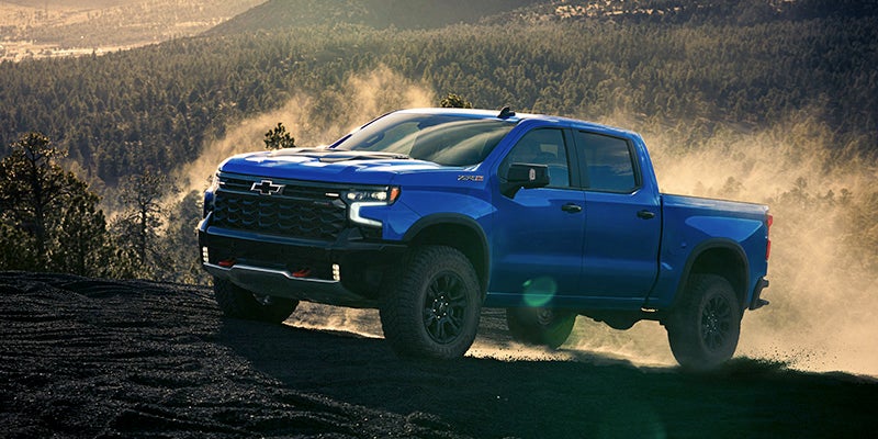 A blue pickup truck drives over a dirt-covered landscape