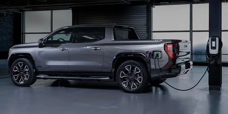 A gray electric pickup truck parked indoors and connected to a wall-mounted charging station