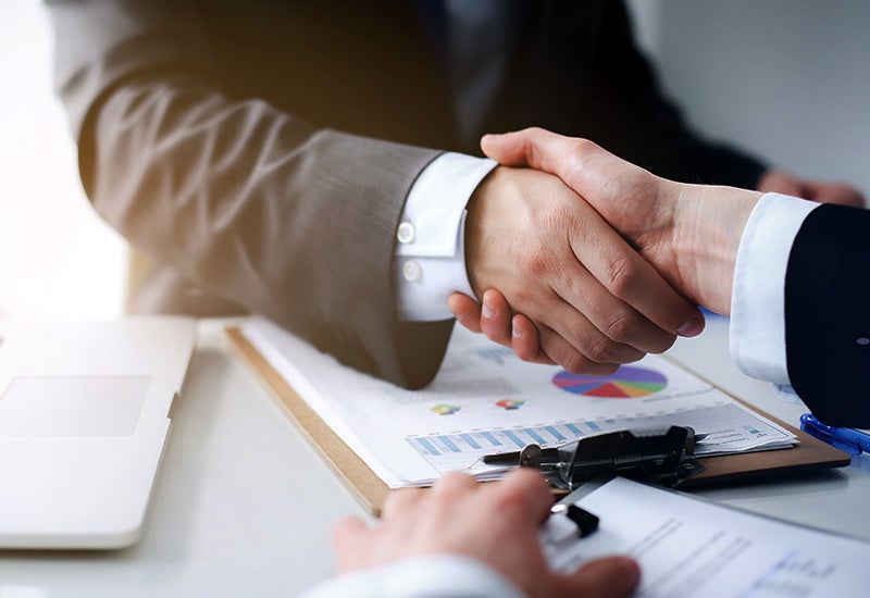 A close-up view of two individuals shaking hands over a desk