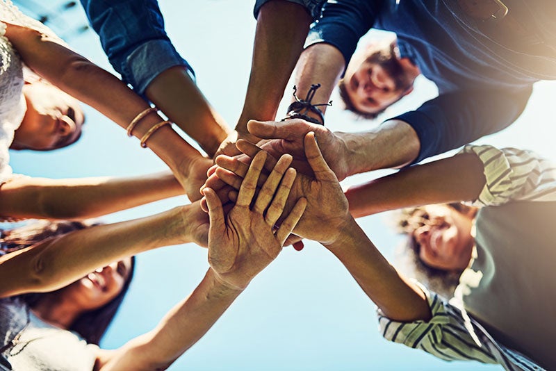 A group of people standing in a circle reach their arms toward the center