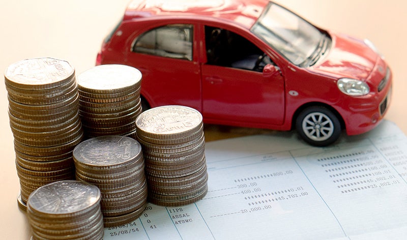 A small red car model positioned beside several stacks of coins on top of a financial document