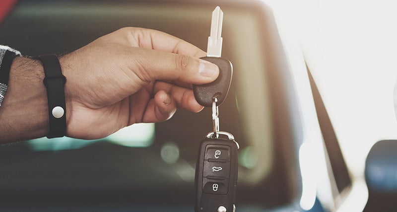A close-up view of a hand holding a car key and key fob in front of a vehicle